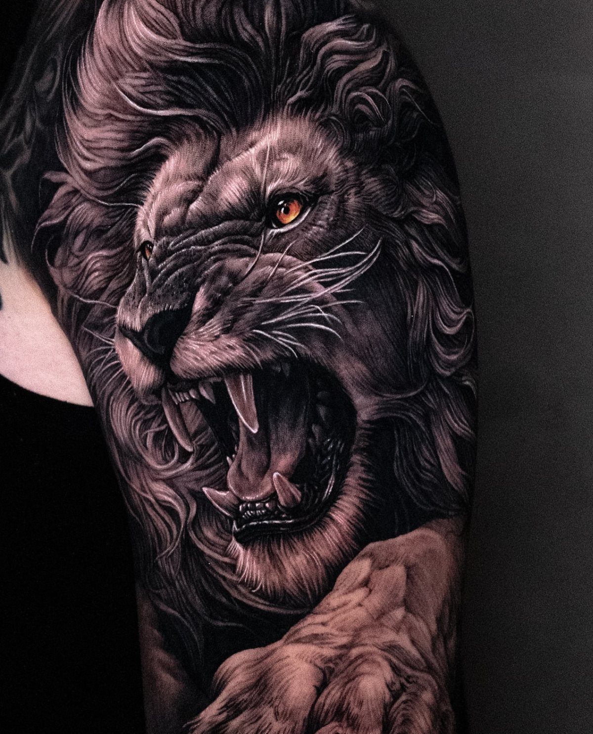 Roaring lion portrait tattoo on an upper arm with striking orange eyes.