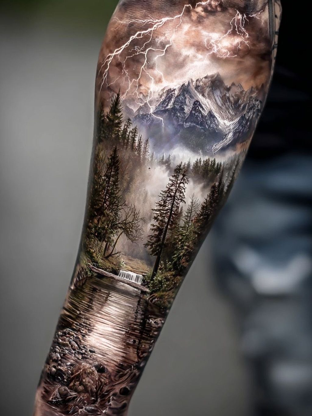 Realistic arm tattoo depicting a mountain landscape with a river and lightning strikes.