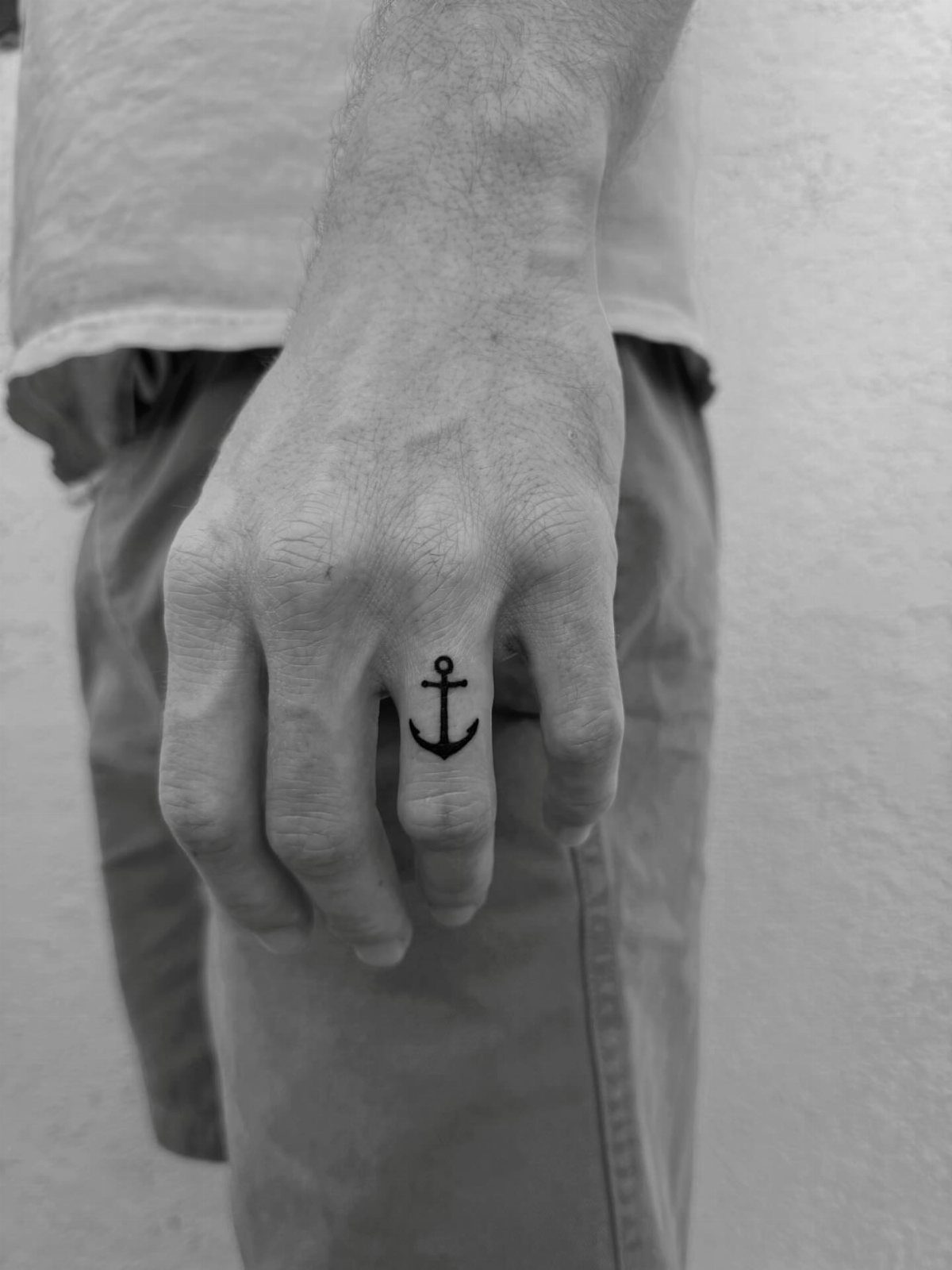 Small black anchor tattoo on the middle finger of a man's hand.