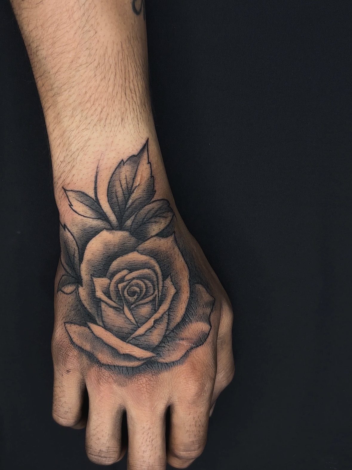 Rose tattoo with leaves on the back of a man's hand.
