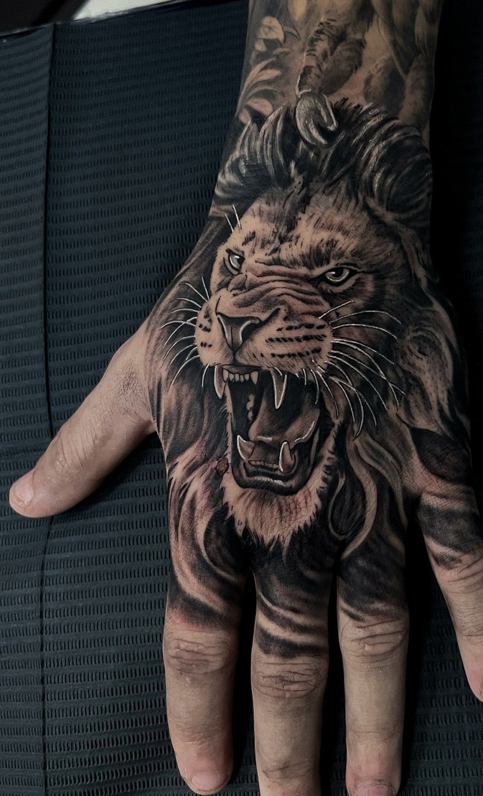 Roaring lion head tattoo in black and grey ink on a man's hand.