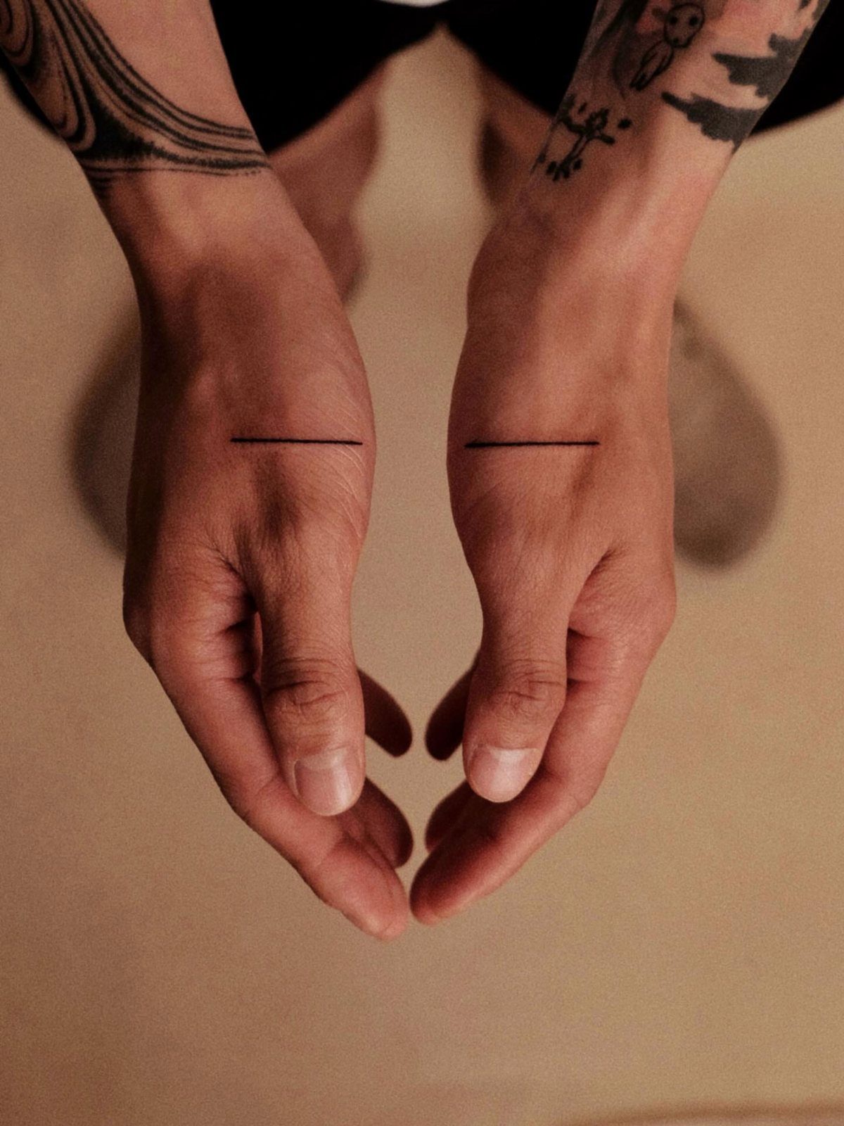 Two hands featuring minimalist thin horizontal black line tattoos on the back.