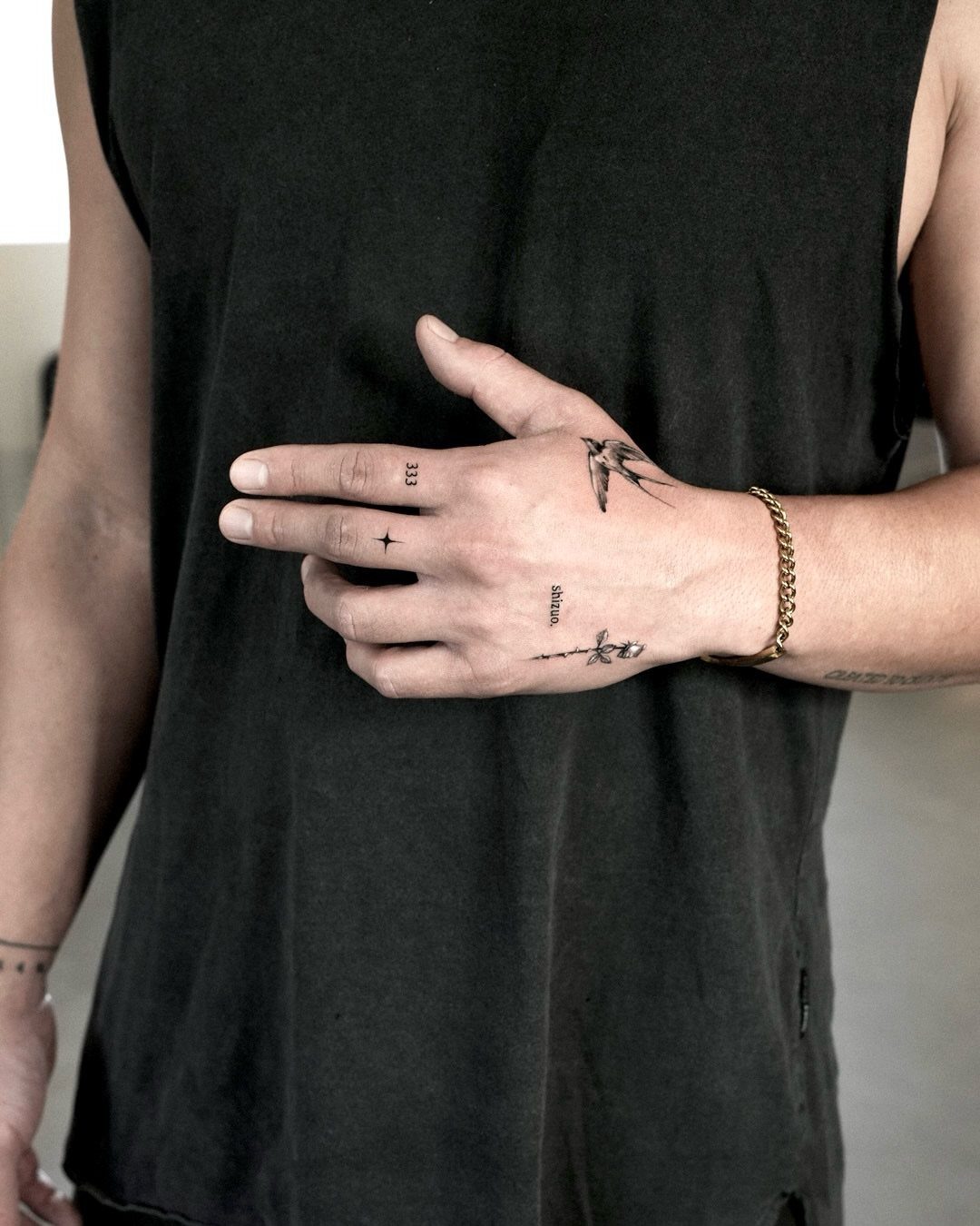 Man's hand featuring several small and simple black ink tattoos and gold bracelet