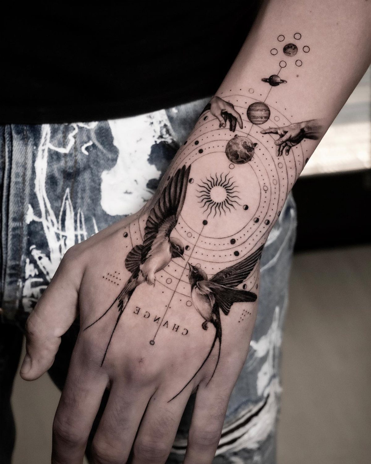 Hand tattoo featuring two swallows and a central sun with celestial planets.