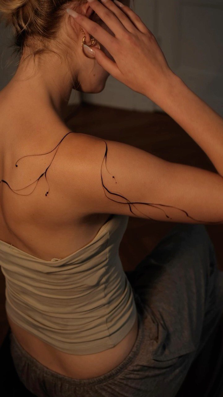 Woman's back and shoulder with a thin black ink abstract line tattoo.