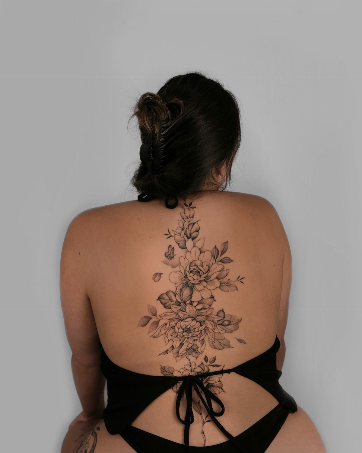 Woman's back with a detailed black ink flower tattoo along the spine