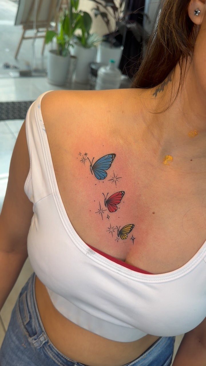 Three colorful butterfly tattoos in blue, red, and yellow on a woman's upper back.