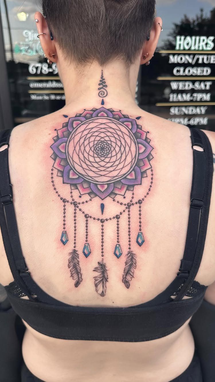Dreamcatcher tattoo with purple mandala and feathers on a woman's upper back