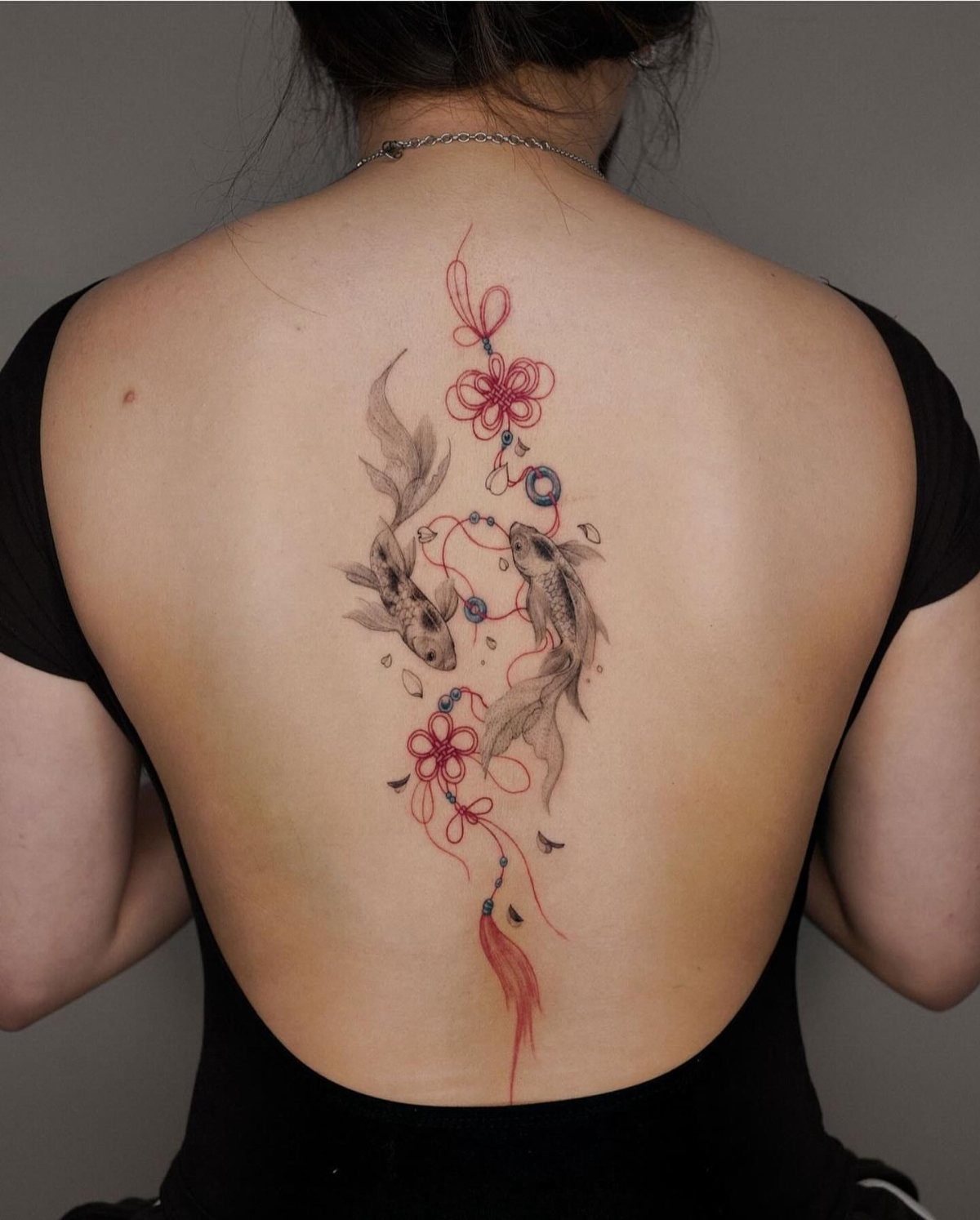 Two koi fish tattoo with red flowers on a woman's back.