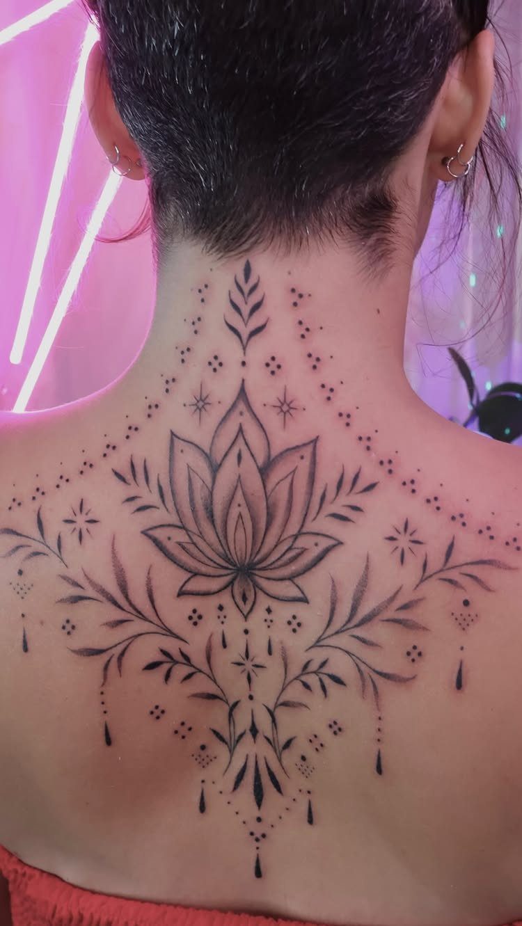 Lotus flower tattoo with ornamental patterns on a person's upper back and neck.