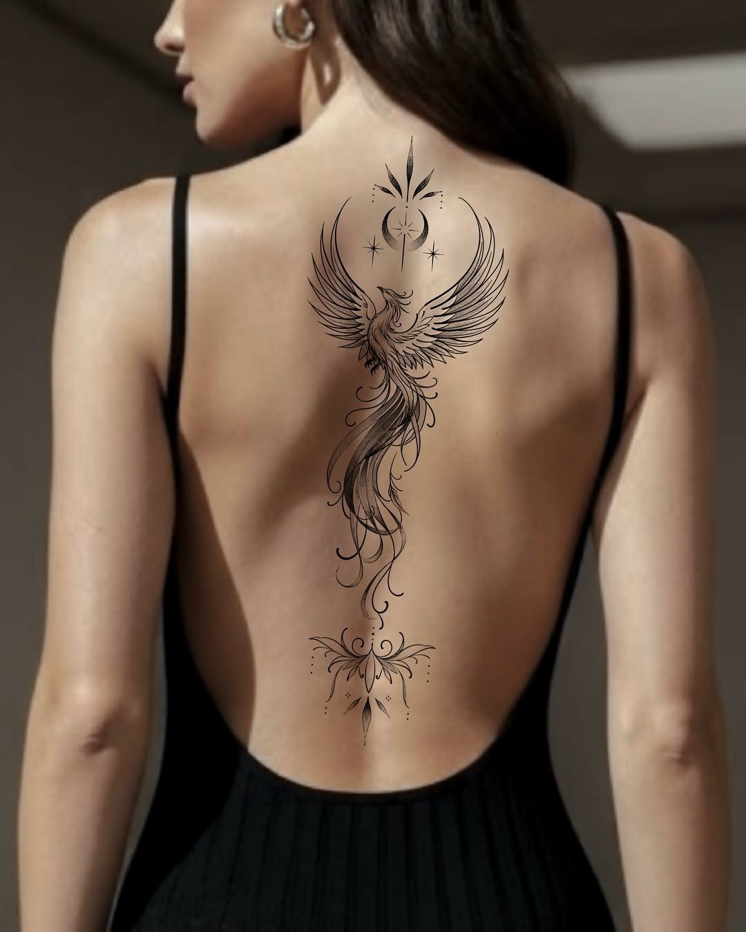 Phoenix tattoo with celestial symbols on a woman's back wearing a black dress