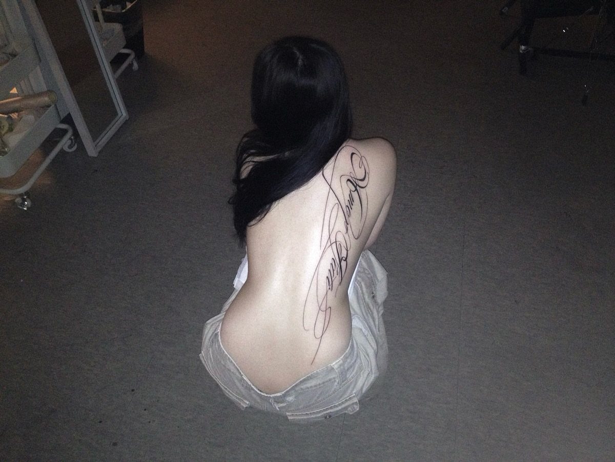 Woman with a long black script tattoo running down her right back.