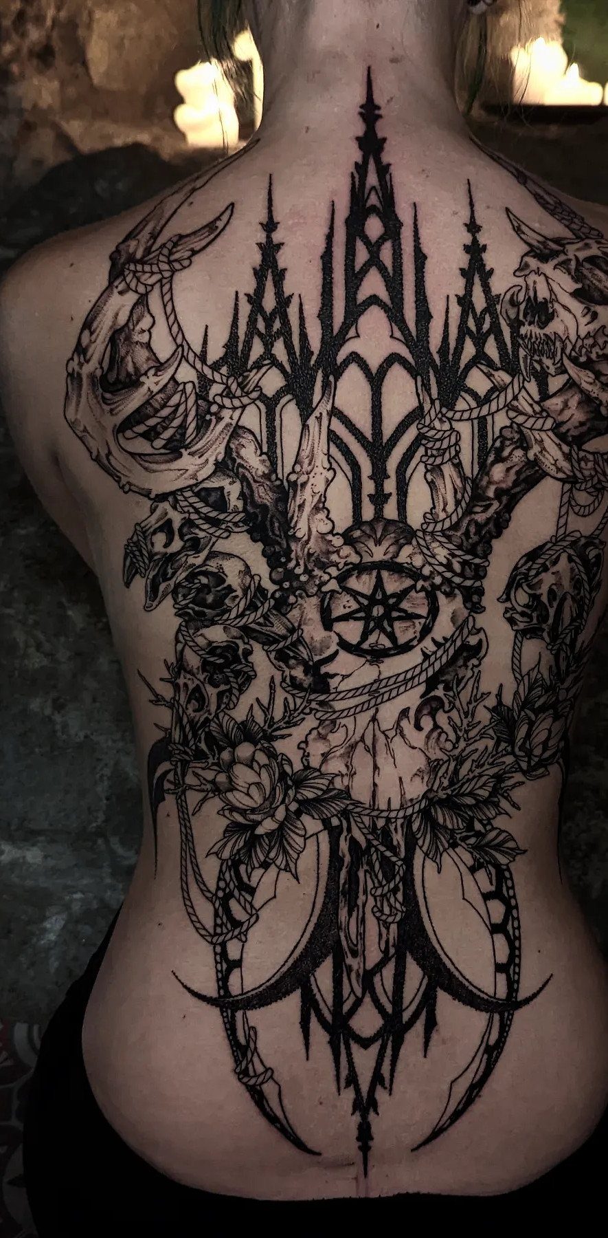 Large black ink gothic tattoo on a woman's back featuring skulls and architecture.