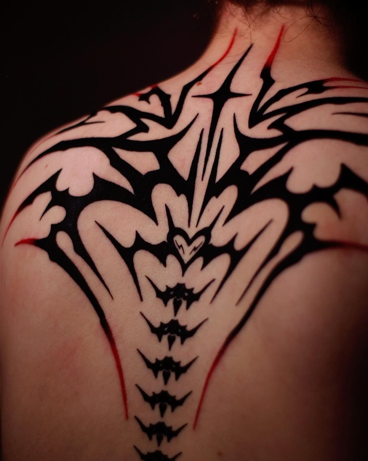 Symmetrical black tribal tattoo with red accents on a person's upper back and spine.