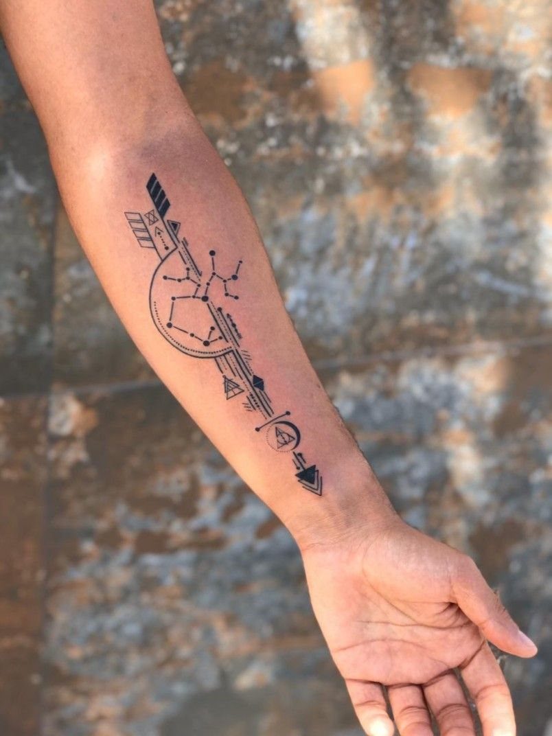 Geometric black ink tattoo with arrows and lines on a lower arm
