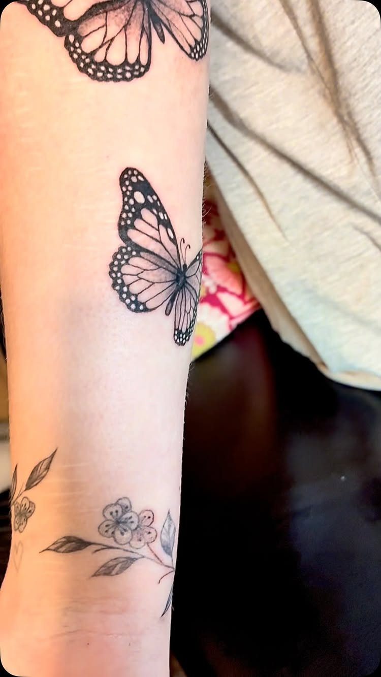 Butterfly tattoos and a floral branch on a person's lower arm.