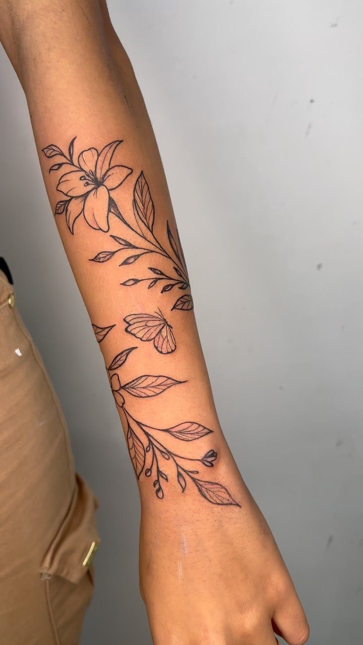 Floral tattoo on a lower arm featuring a lily and a small butterfly.