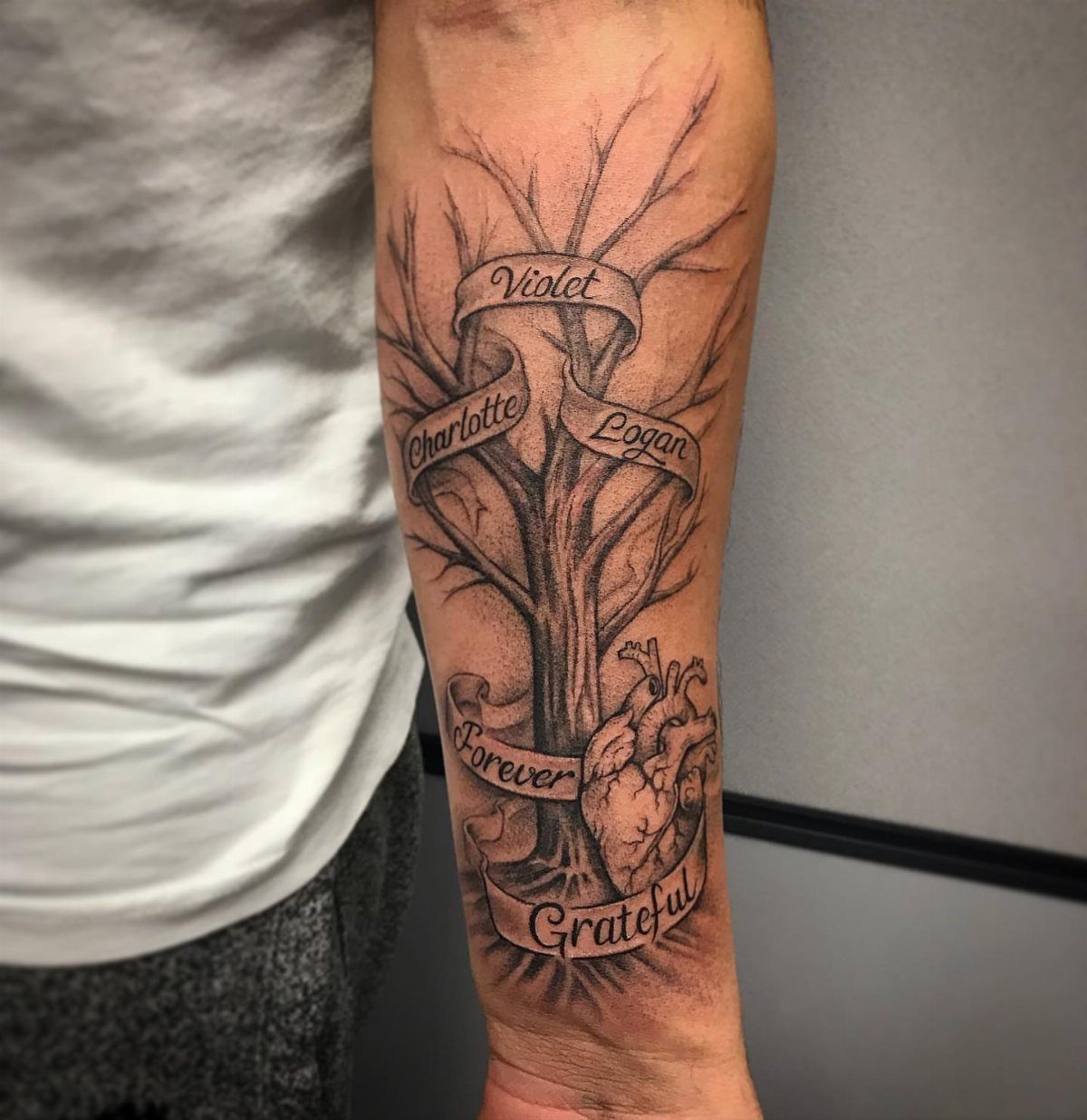 Tree of Life tattoo on a forearm with banners and an anatomical heart