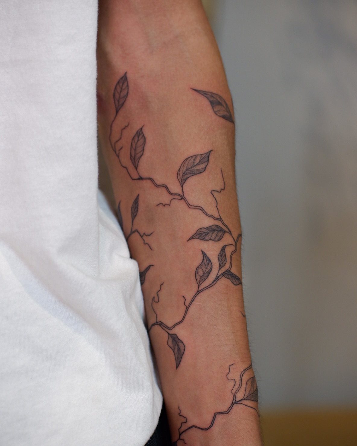 Vine and leaf tattoo wrapping around a person's lower forearm