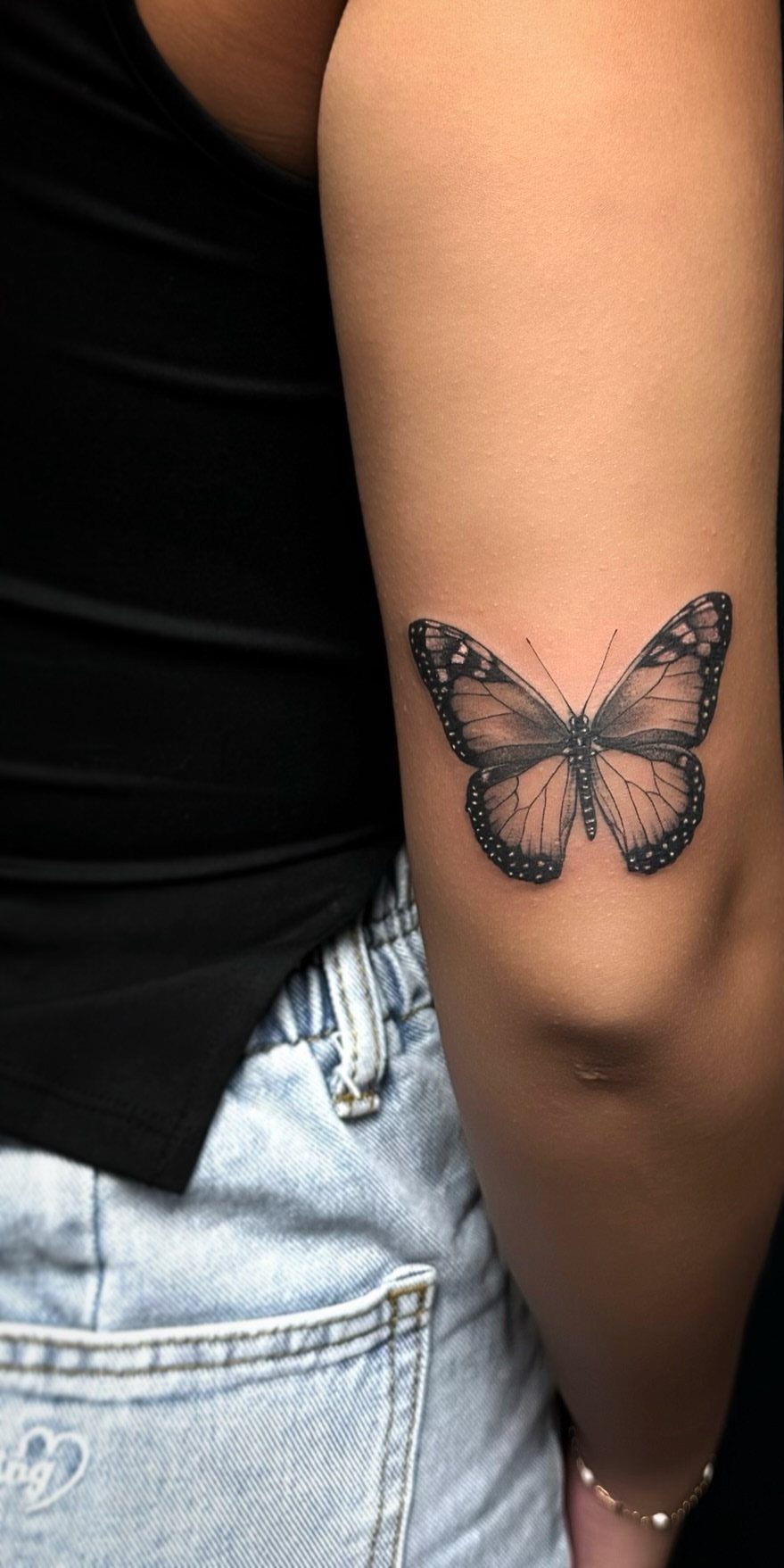 Butterfly tattoo on a person's upper arm with detailed wings and shading.