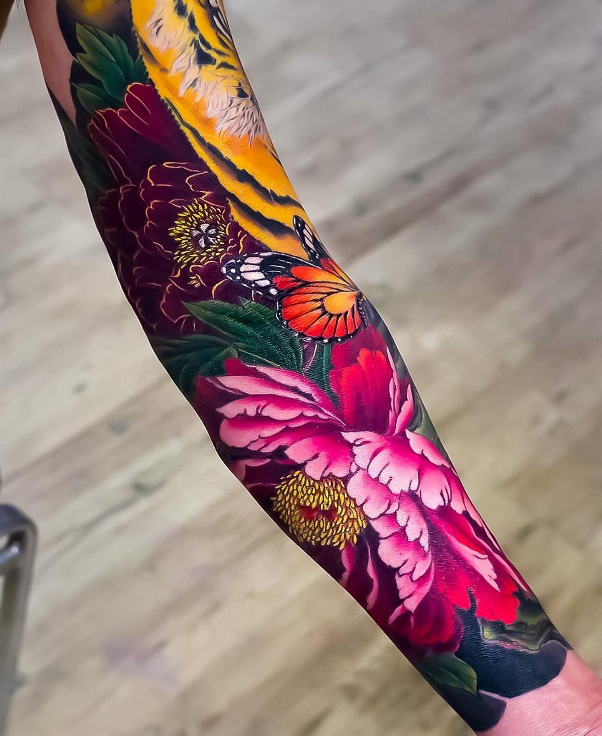 Floral arm sleeve tattoo with red peonies, an orange butterfly, and a tiger.