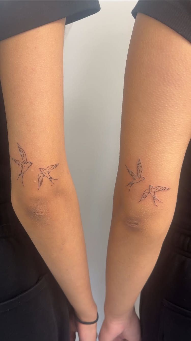 Two matching tattoos of small birds in flight on two separate forearms.