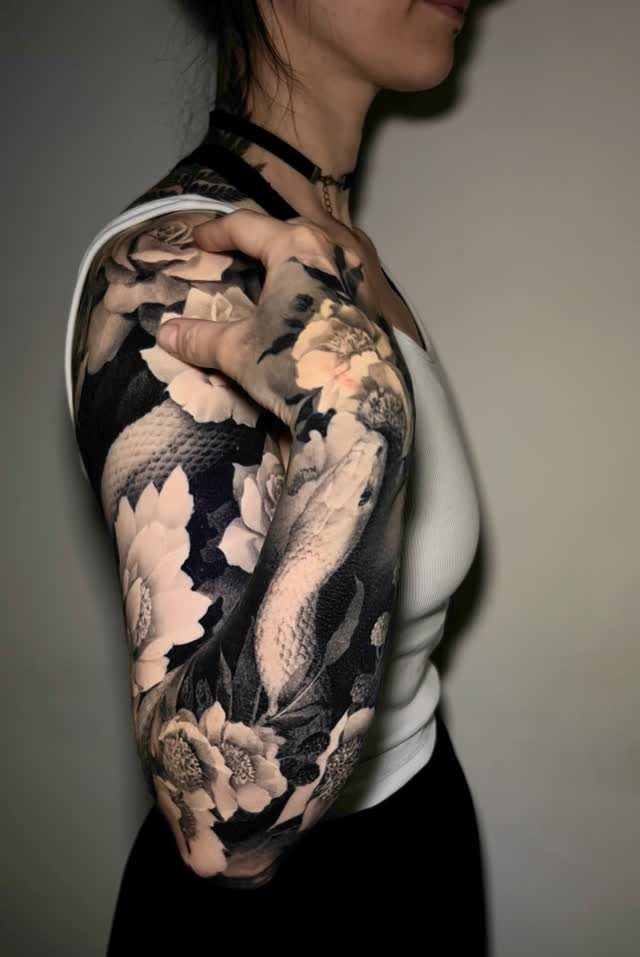 Woman's arm with a detailed black and grey snake and flower tattoo.