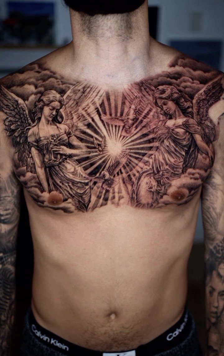 Detailed black and grey chest tattoo featuring two angels and radiant light beams.