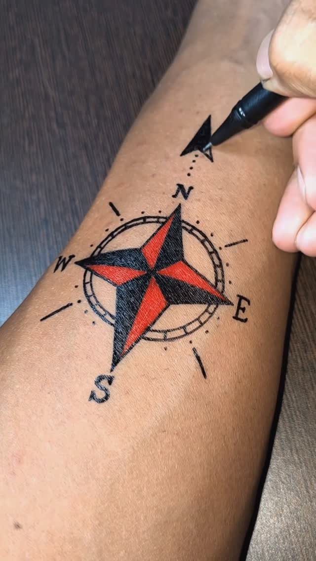 Compass tattoo with red and black star on a forearm being sketched above