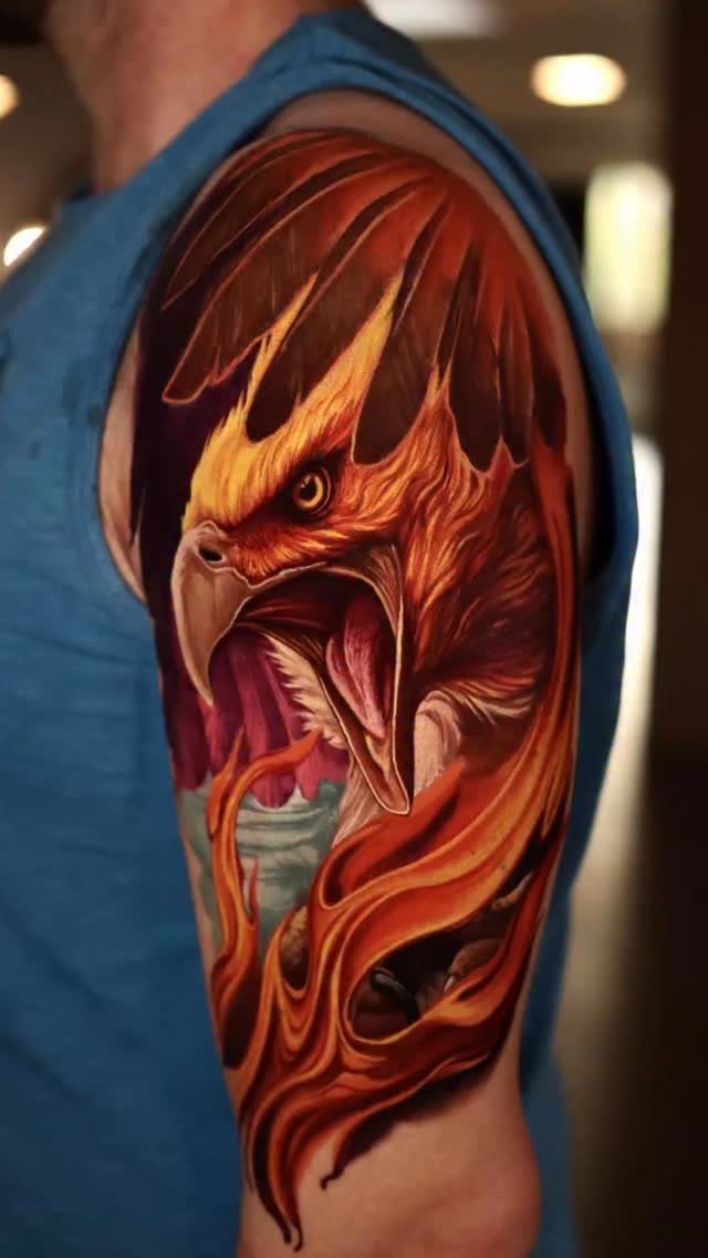 Phoenix tattoo with fiery orange and red feathers on a man's upper arm.