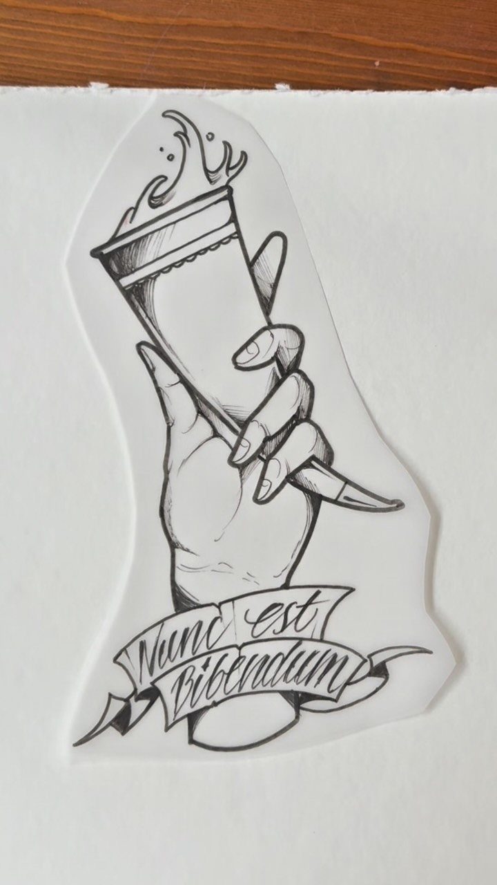 Hand holding a glass with a splash and a Latin quote tattoo sketch.