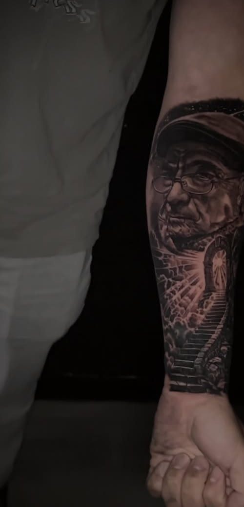 Realistic portrait tattoo of an older man with glasses on a forearm