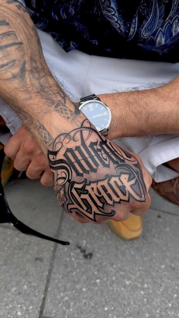 Black ink script tattoo on the back of a man's hand and knuckles