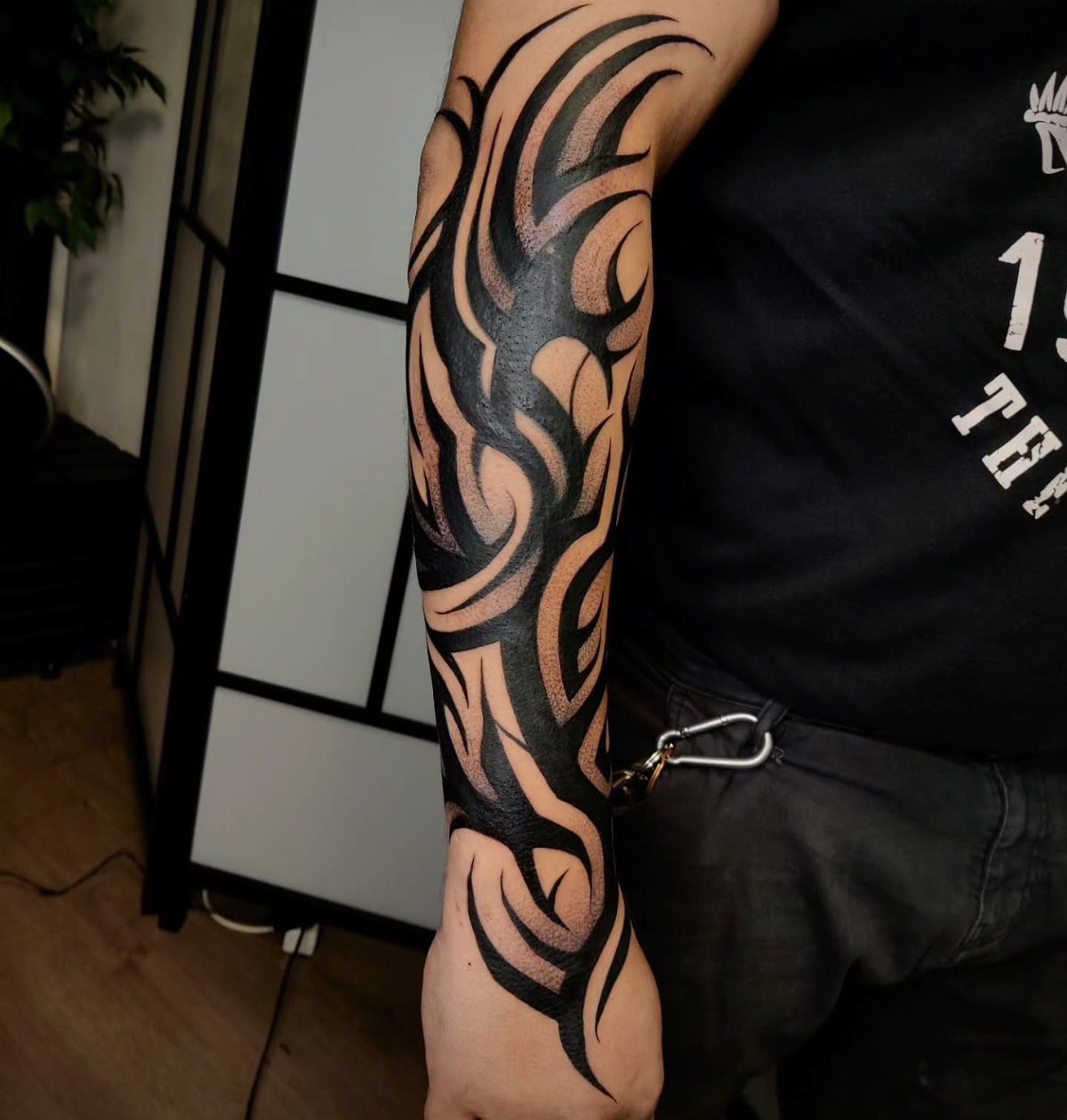 Bold black tribal tattoo with curved patterns on a man's forearm