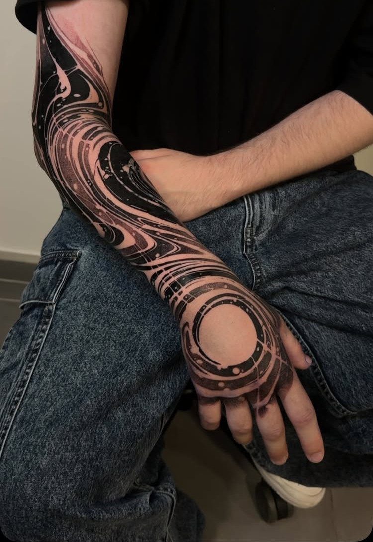 Abstract black and grey swirling tattoo sleeve covering a man's arm and hand.
