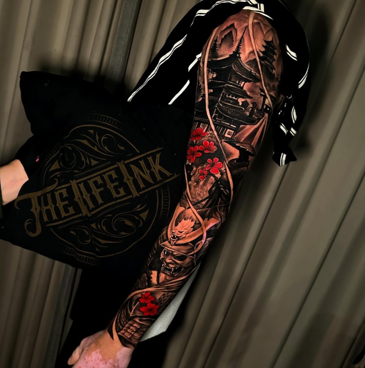 Full sleeve tattoo featuring a Japanese pagoda, red flowers, and a skull.