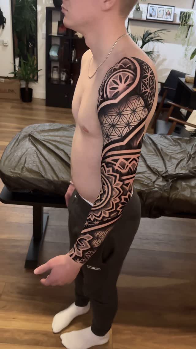 Man with a full sleeve tattoo featuring black geometric patterns and mandalas.