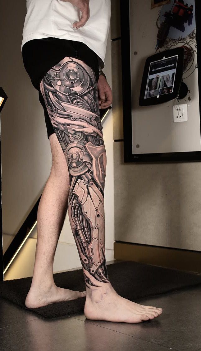 Biomechanical tattoo sleeve on a leg featuring intricate gears and mechanical parts.