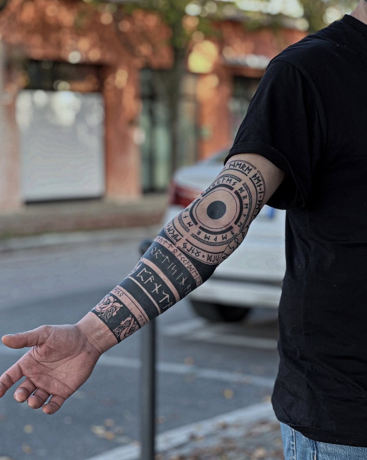 Man's arm with a black ink Nordic Viking sleeve tattoo featuring runes and circles.