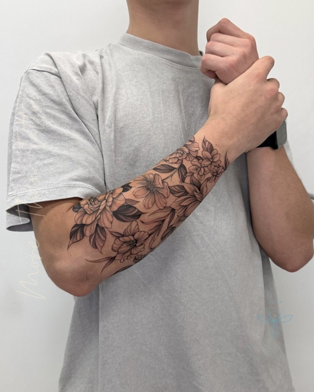 Floral tattoo sleeve on a man's forearm featuring detailed black and grey blossoms.