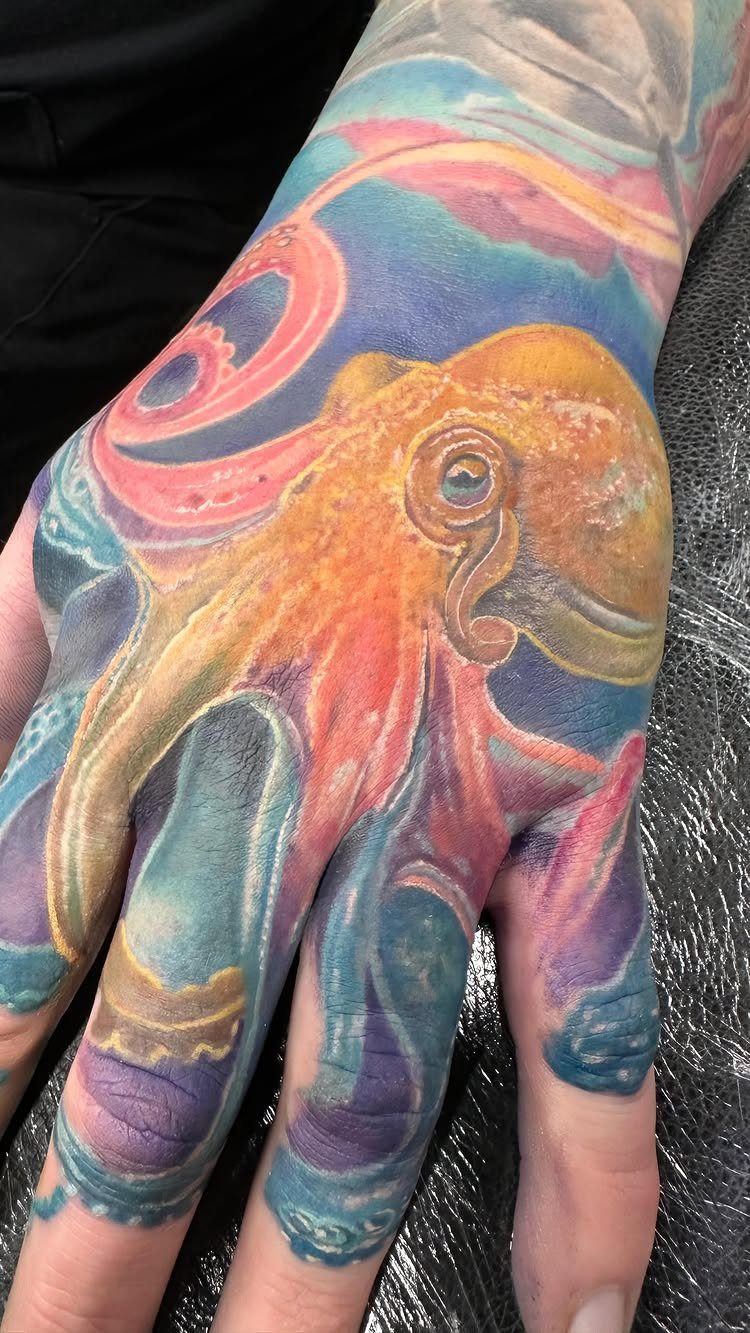Octopus tattoo with vibrant orange and blue watercolor style on a person's hand.