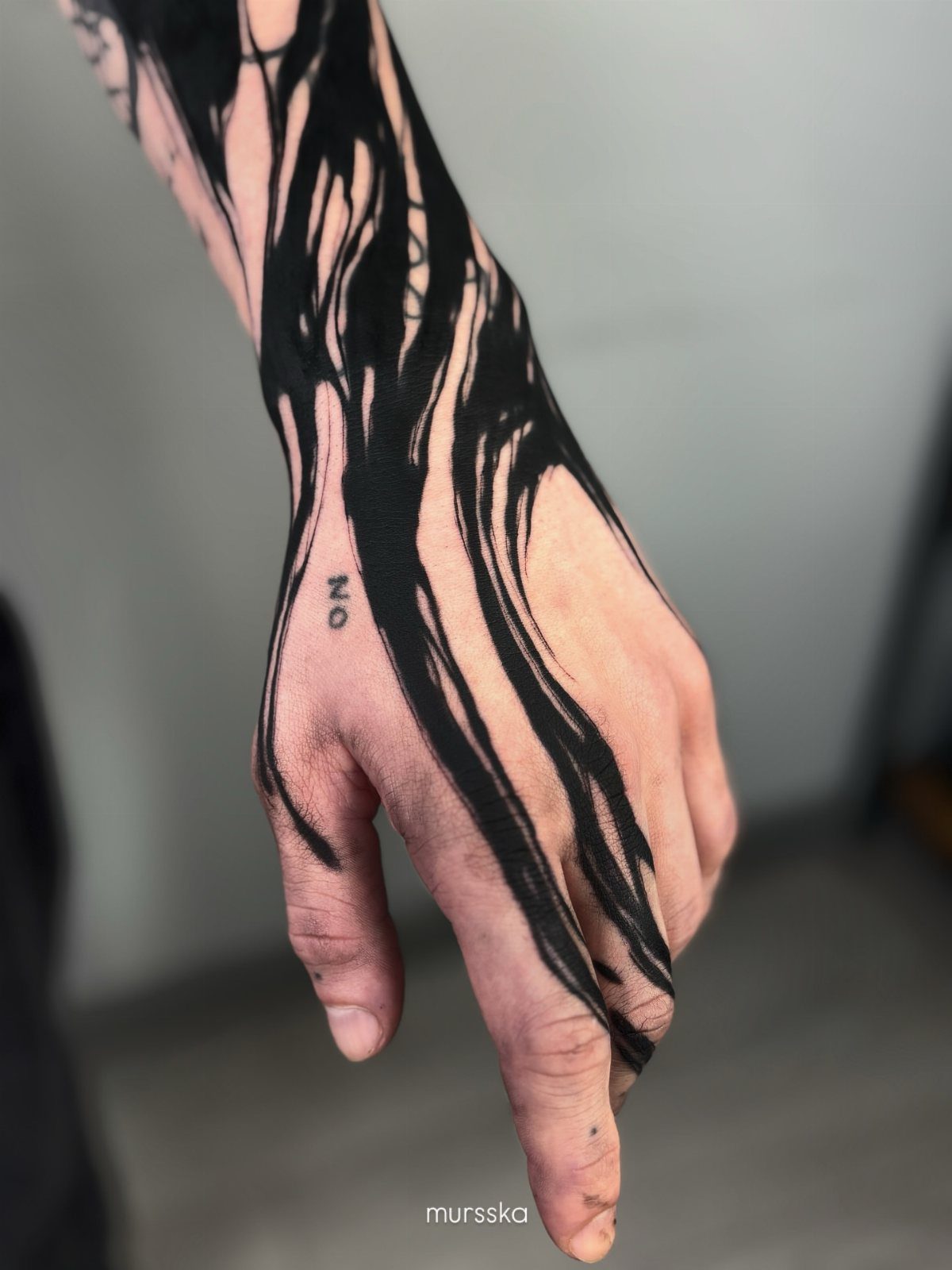 Hand and wrist with bold black abstract flowing ink tattoos and small text.