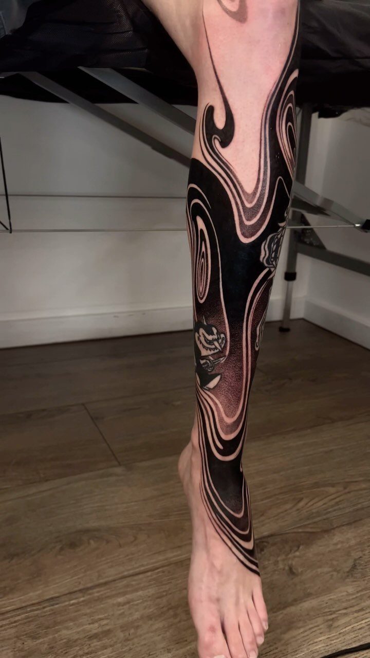 Lower leg and foot with a bold blackwork tattoo of flowing organic shapes.