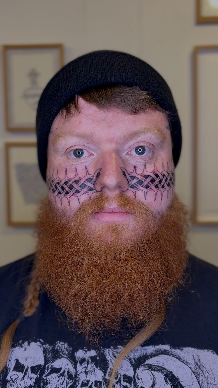 Man with red beard and black knotwork tattoos across his cheeks and nose.