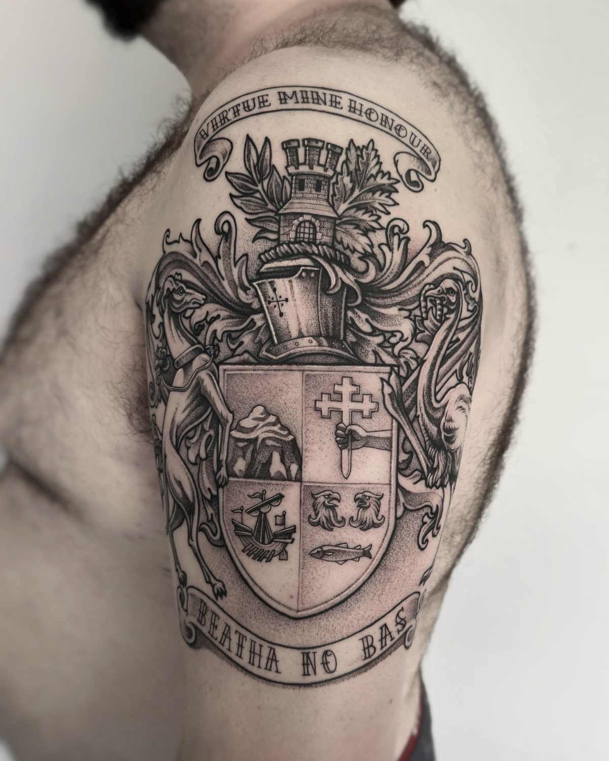 Detailed family crest tattoo on a man's upper arm with heraldic symbols and banners.