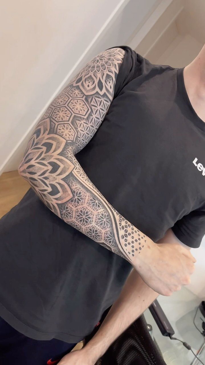 Full sleeve tattoo with black geometric patterns and mandalas on a man's arm.