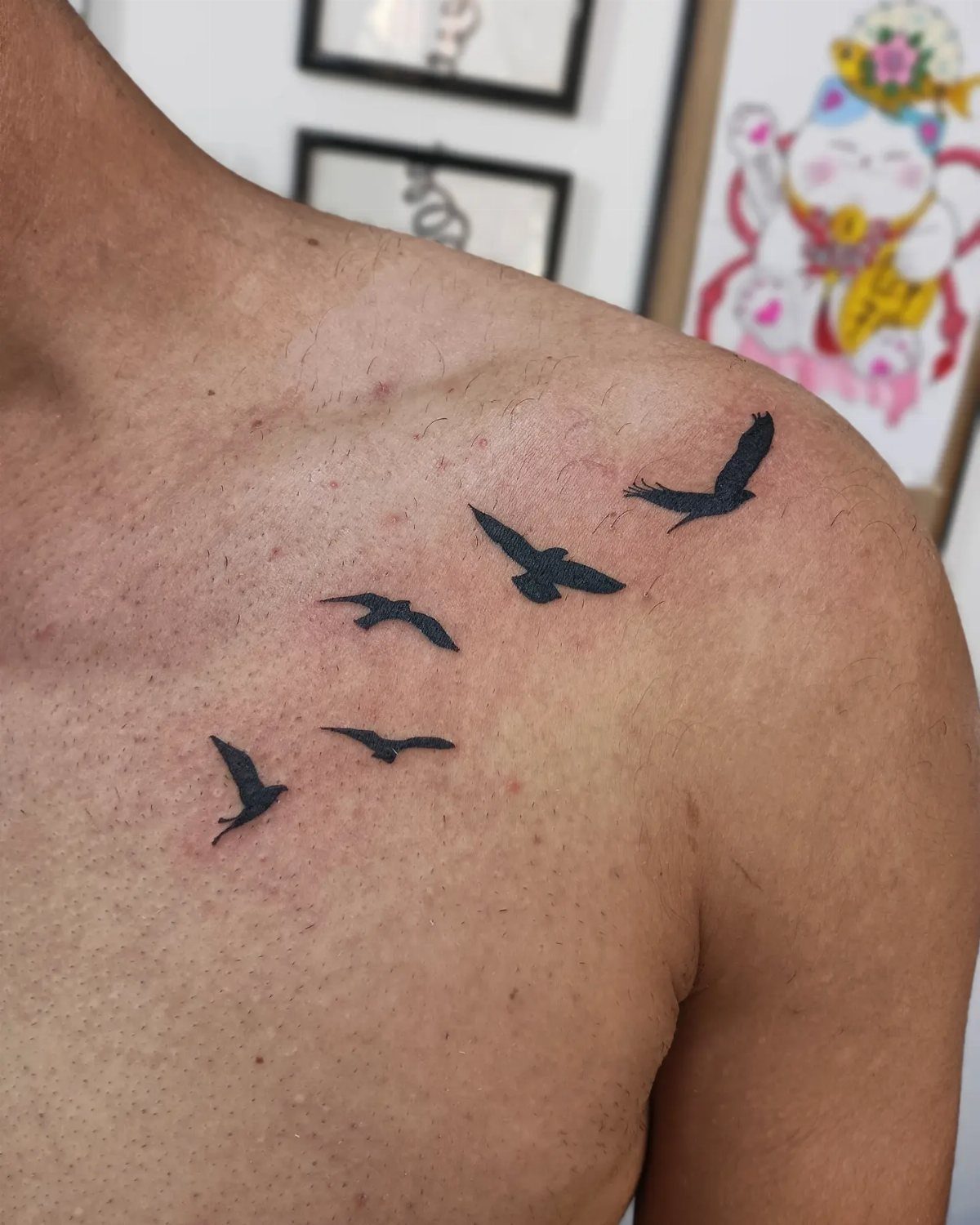 Six small black bird silhouette tattoos flying across a man's shoulder and chest.
