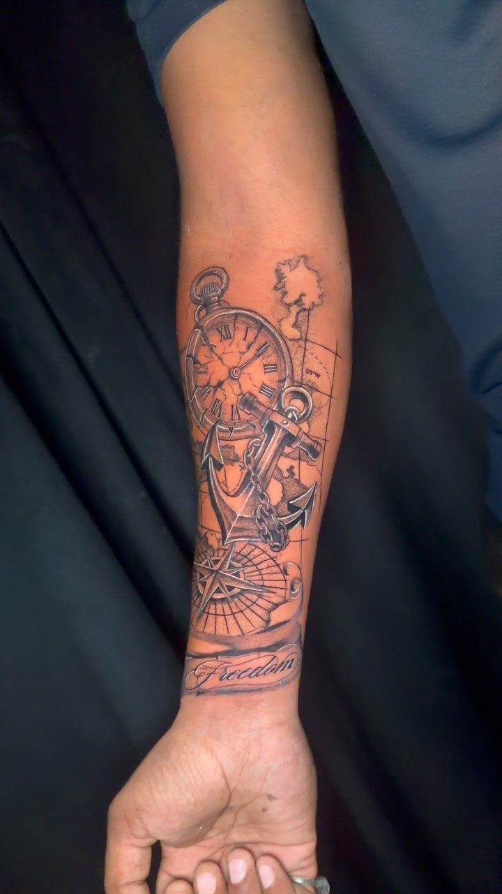 Nautical tattoo on a forearm featuring an anchor, pocket watch, and a compass.
