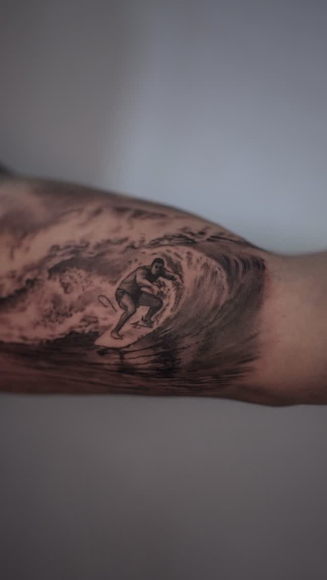 Surfer riding a curling ocean wave tattoo in black and grey realism style.