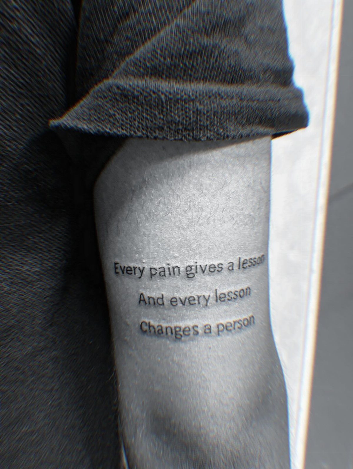 Arm tattoo with a quote about pain, lessons, and personal change in black ink.